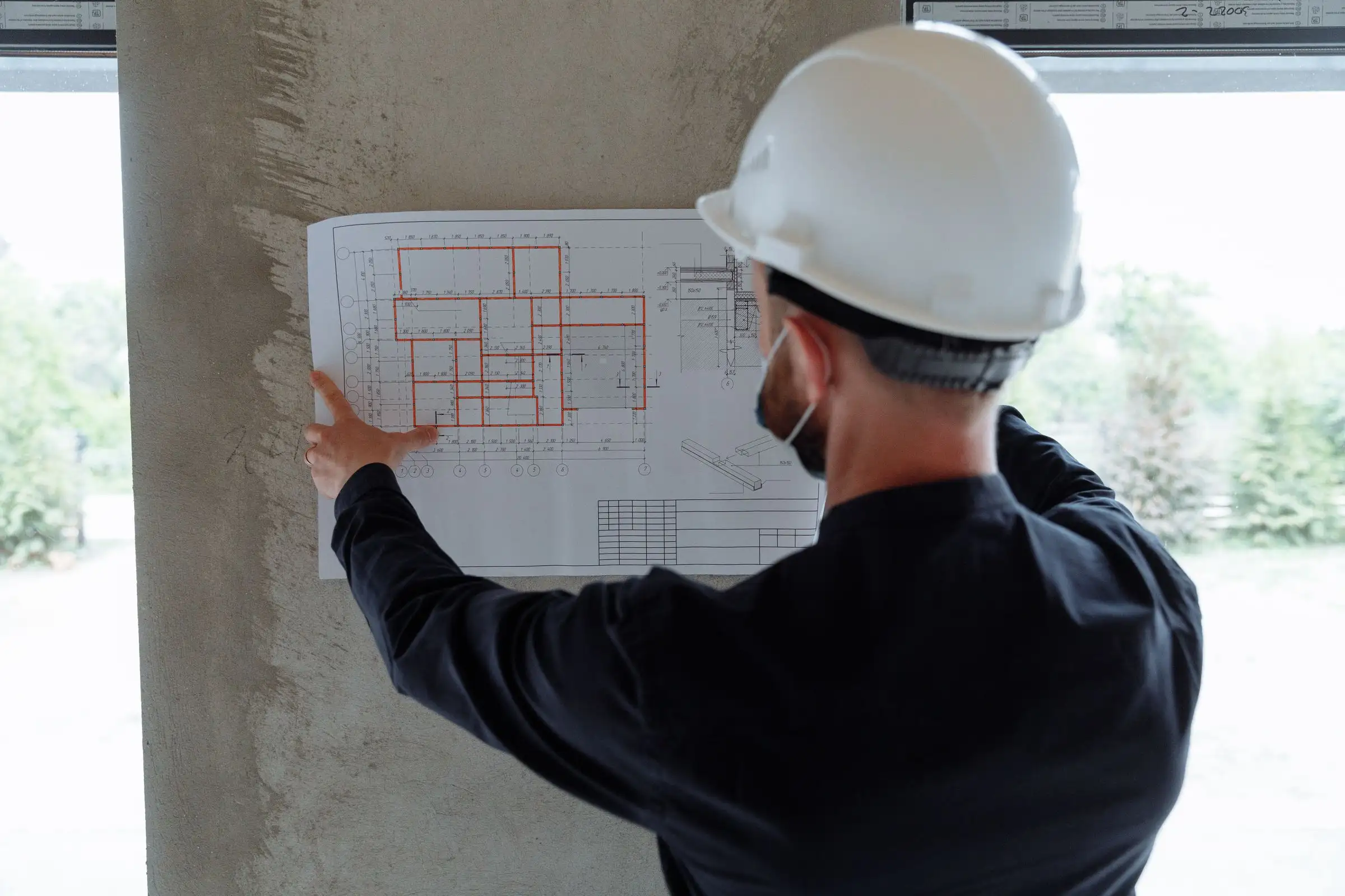 Project manager seen from behind, holding a plan against a wall