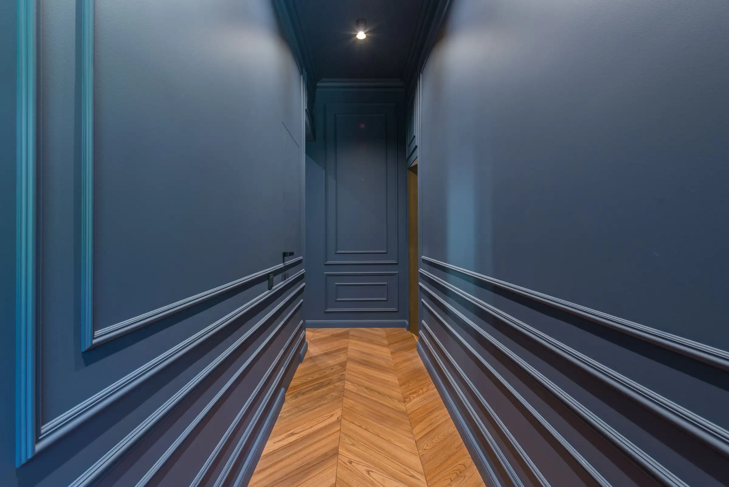Couloir peint en bleu profond, plinthes hautes et parquet en chevrons
