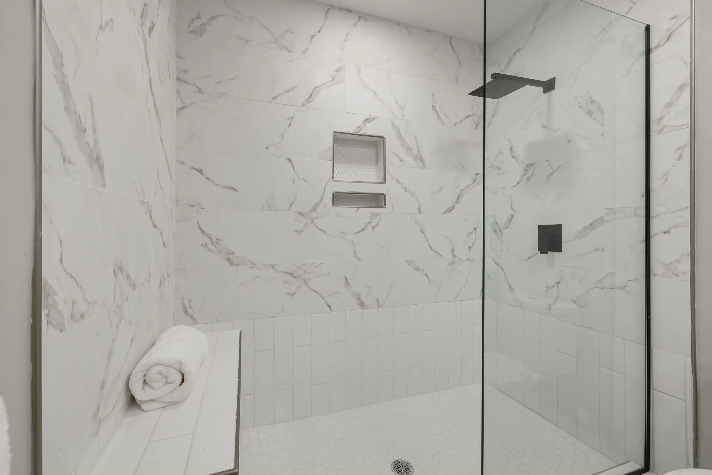 Douche de plain-pied en grès effet marbre, paroi vitrée et niche