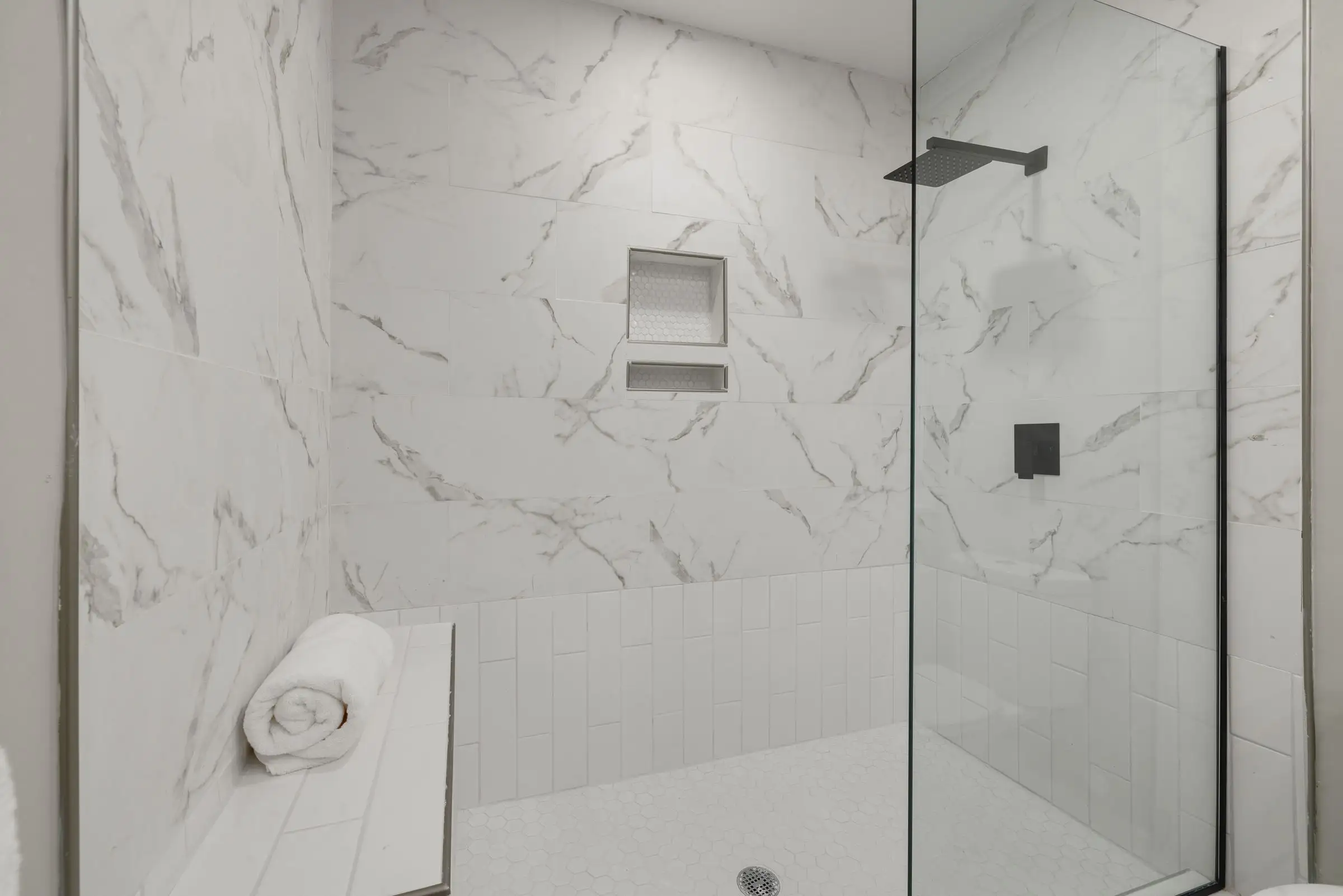 Douche de plain-pied en grès effet marbre, paroi vitrée et niche