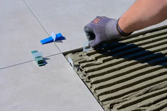 Carreleur posant de grands carreaux gris avec des croisillons de nivellement