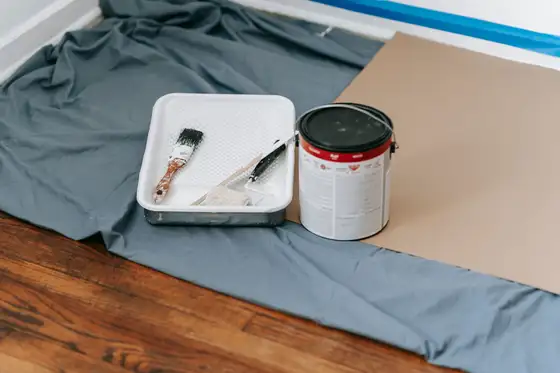 Bâche de protection et pot de peinture posés sur un parquet