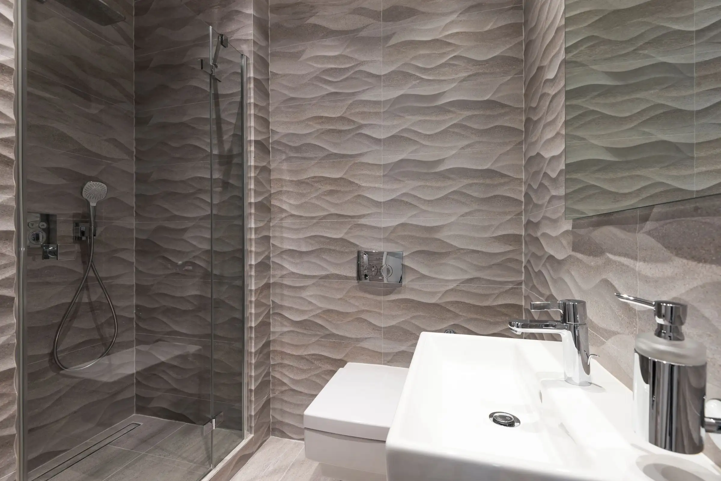 Salle de bains au carrelage gris à relief en vagues, douche et vasque blanche